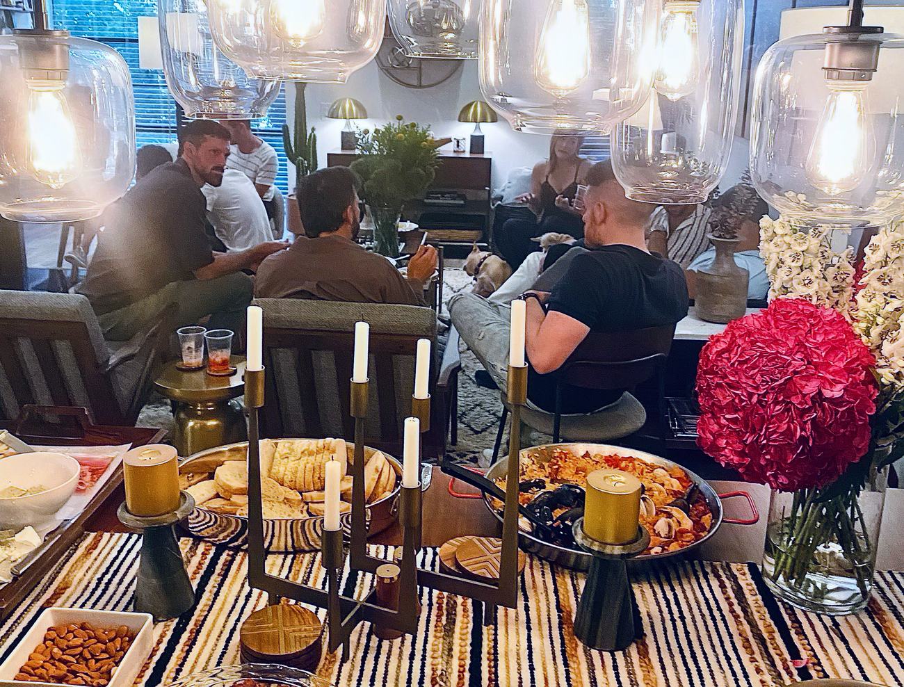 Guests gathered on couches after dinner in a Los Angeles home, the table still set in the foreground beneath warm pendant light